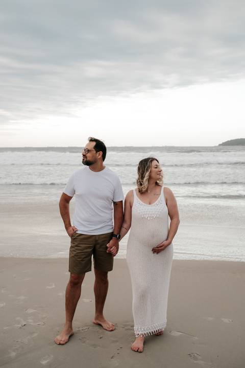 Foto do casal posando de frente para a câmera na areia molhada.'