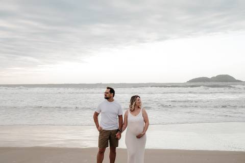 Foto panorâmica do casal centralizado na praia durante o entardecer.'