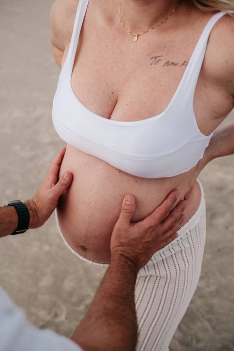 Foto de detalhe das mãos do pai e da mãe repousando sobre a barriga.'