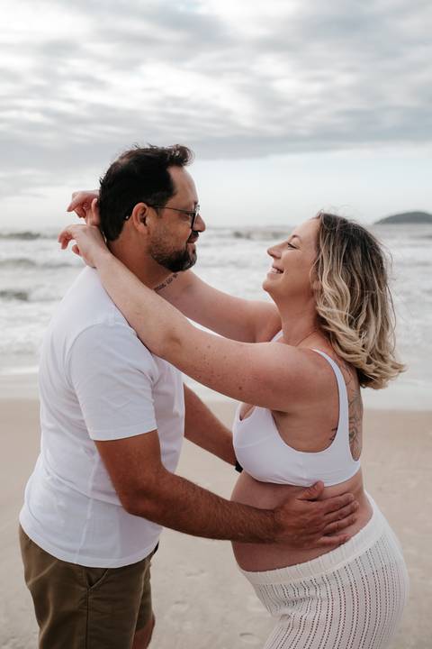Foto do casal abraçado e rindo, com a gestante envolvendo o pescoço do parceiro.'