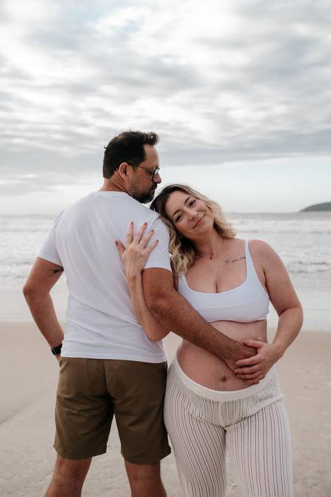 Foto do casal posando de costas um para o outro, com a gestante olhando para a câmera.'