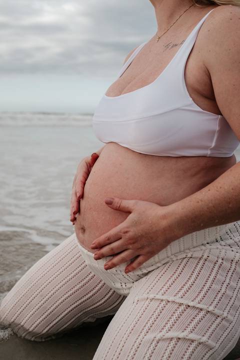 Close lateral da barriga da gestante com as mãos repousadas suavemente.'
