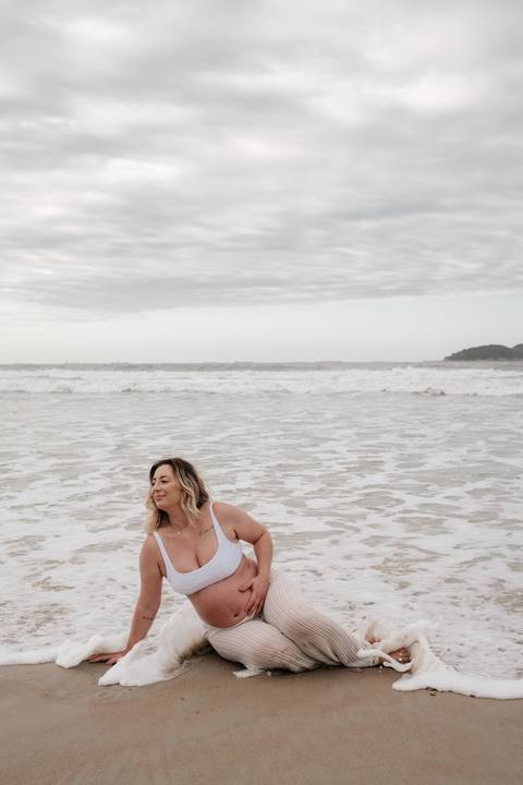 Foto aproximada da gestante relaxando na beira d'água durante a maré baixa.'