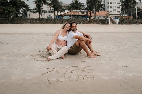 Foto do casal sentado na areia atrás da inscrição 