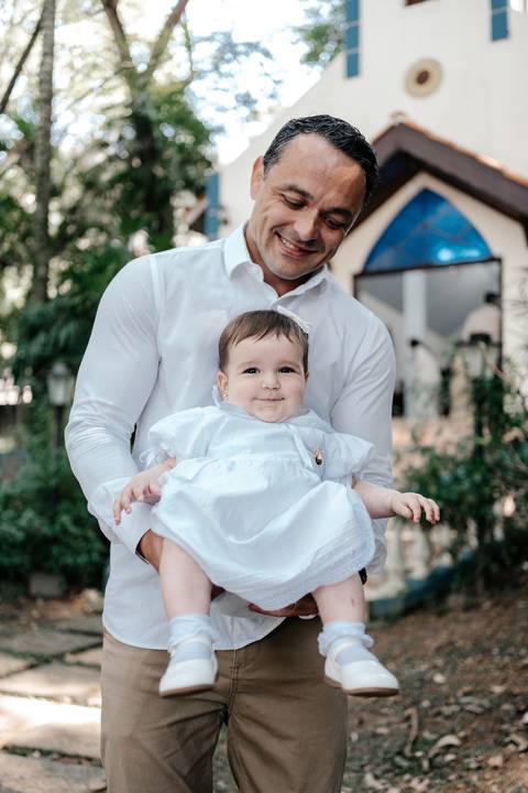 Foto aproximada do pai segurando a bebê, que olha diretamente para a câmera.'