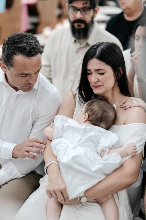 Foto da mãe emocionada com lágrimas no rosto, amparada pelo marido enquanto segura a filha.'