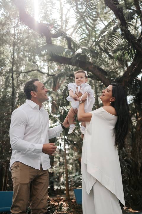 Foto do casal erguendo o bebê no ar em momento de alegria e celebração.'