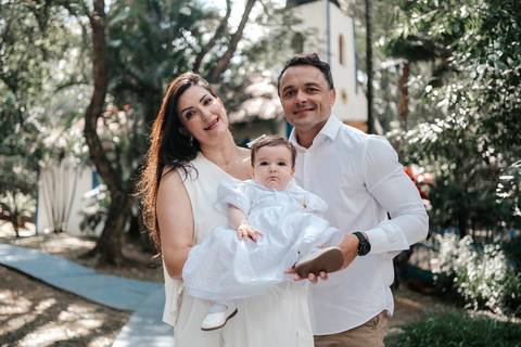 Retrato do casal com a mãe segurando a bebê de mandrião, posando no jardim da igreja.'