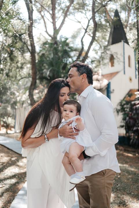 Retrato carinhoso com os pais inclinados dando um beijo na cabeça da pequena.'