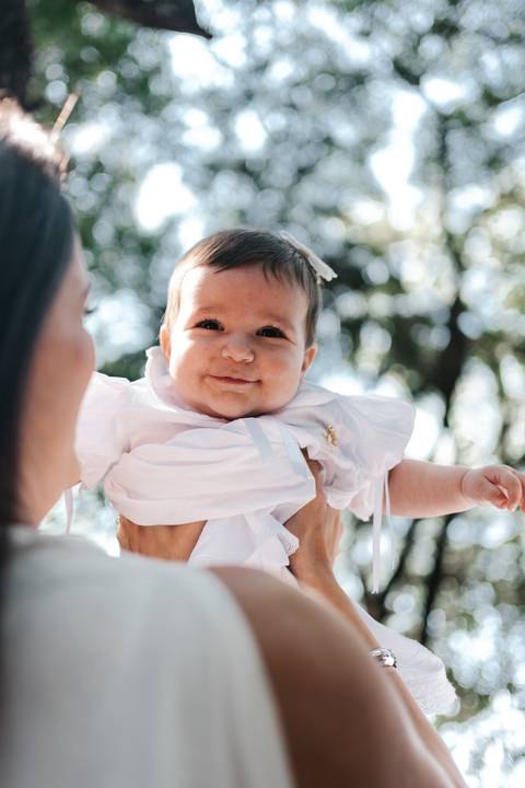 Close da bebê sorrindo de perfil no colo da mãe durante o evento.'