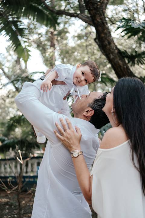 Foto do pai erguendo a bebê no ar, que sorri olhando para ele com carinho.'