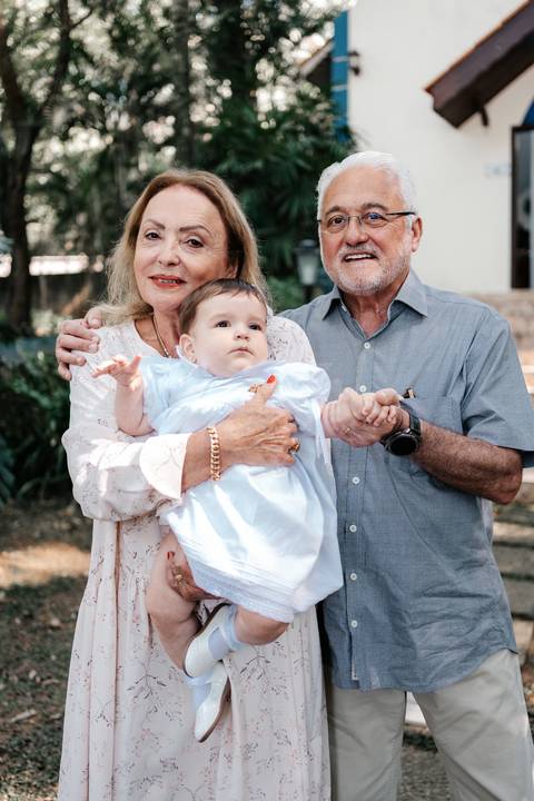 Foto da bebê no colo dos avós emocionados antes de entrar para a cerimônia.'