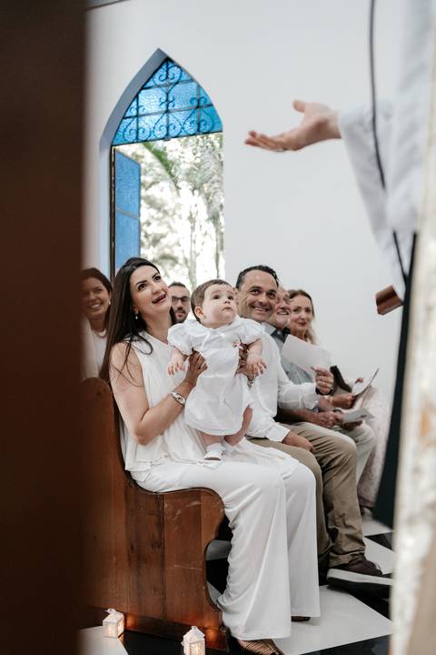 Foto da família sentada no banco da igreja durante o início da celebração.'