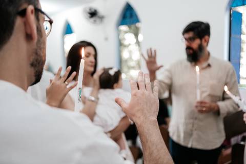 Foto dos pais e padrinhos segurando velas acesas e erguendo as mãos em sinal de benção.'