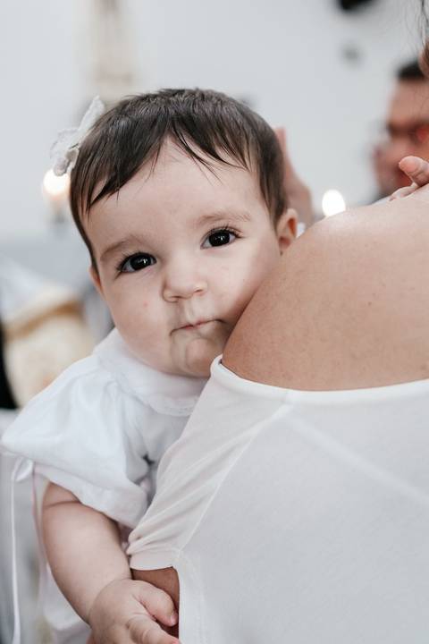 Close da bebê olhando tranquilamente por cima do ombro da mãe durante os ritos.'
