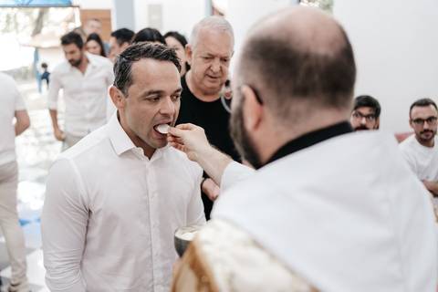 Foto do pai recebendo a hóstia sagrada durante o rito da comunhão.'