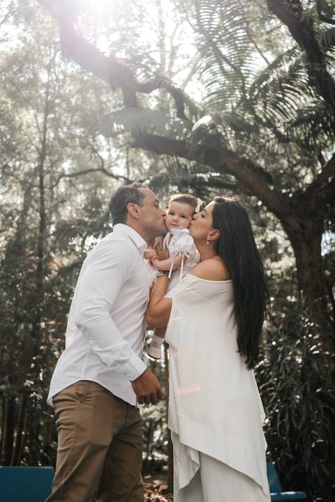 Foto carinhosa do casal beijando simultaneamente as bochechas da filha.'