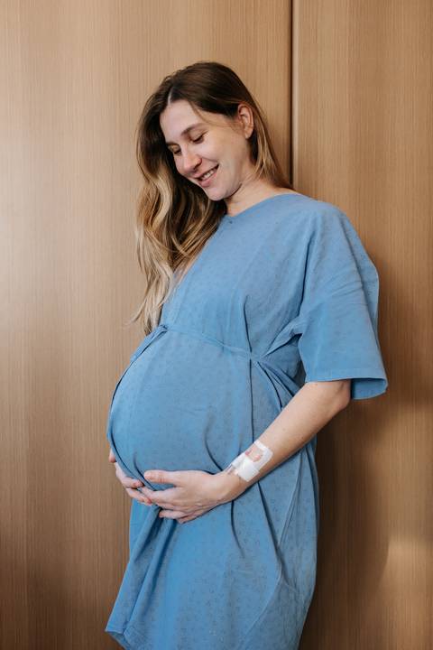 Foto aproximada de perfil da gestante com camisola azul, acariciando a barriga.'