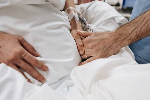 Detalhe do toque e apoio das mãos do casal sobre o leito hospitalar.'