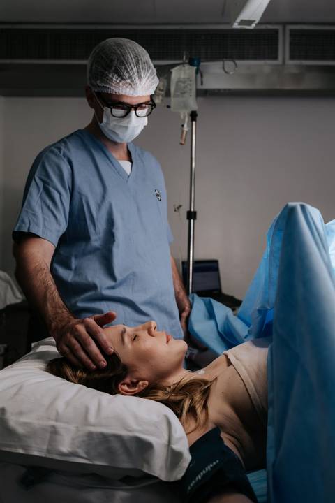 Foto do parceiro acariciando a testa da gestante com carinho durante o procedimento.'