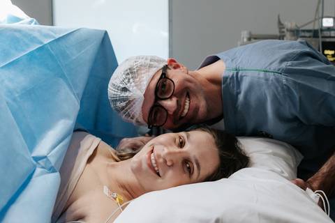 Foto do casal trocando olhares e sorrisos de cumplicidade por trás dos campos cirúrgicos.'