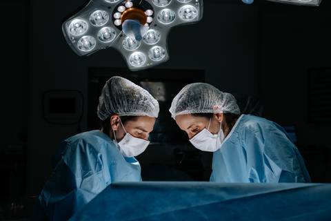 Foto com iluminação dramática focando na equipe médica concentrada durante o parto.'