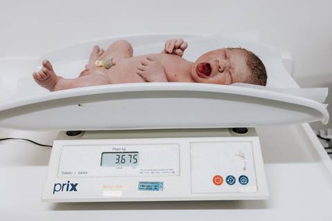 Foto do bebê bocejando na balança pediátrica digital durante sua primeira pesagem.'