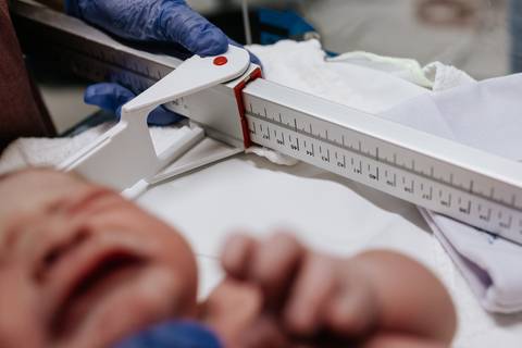Foto em detalhe do recém-nascido chorando durante a medição de estatura no hospital.'