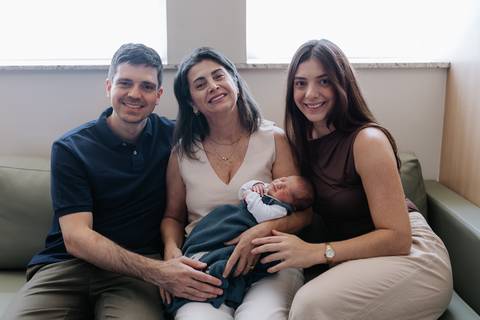 Retrato da avó e dos tios reunidos no sofá com o bebê recém-nascido.'