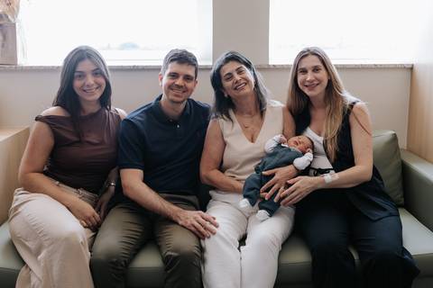 Outro registro da família reunida sorridente com o recém-nascido no colo.'