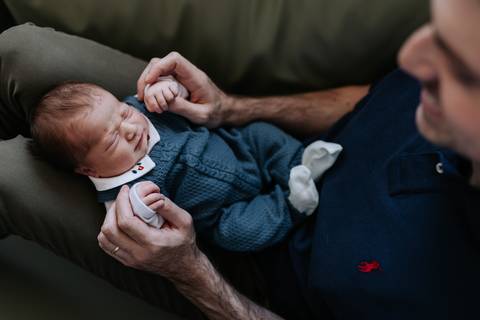 Foto de ângulo superior do pai com o bebê deitado em suas pernas, trocando um momento de carinho.'