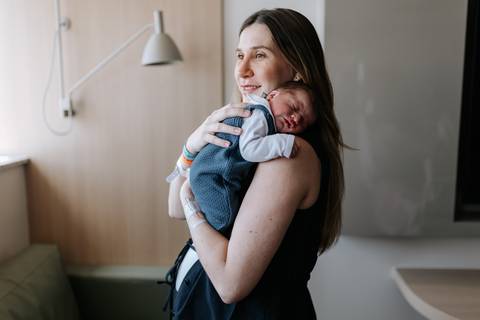 Foto da mãe em pé, abraçando e acalentando o bebê apoiado em seu ombro.'