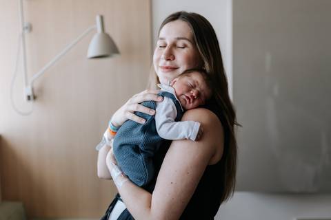 Foto da mãe de olhos fechados, aproveitando o momento com o filho no colo.'
