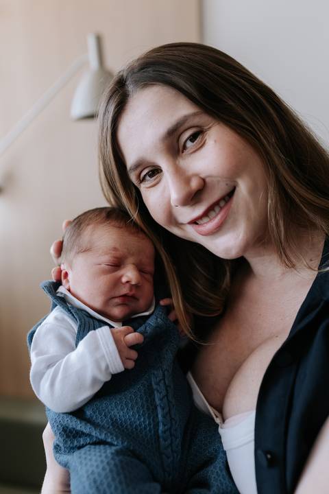 Retrato aproximado da mãe sorridente com o rosto colado ao do bebê adormecido.'