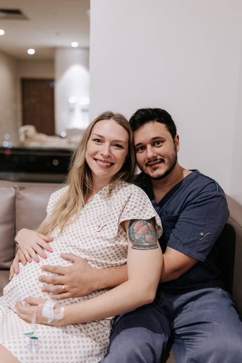 Retrato do casal abraçado no sofá, transmitindo cumplicidade e expectativa.'