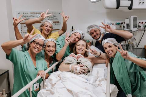 Retrato descontraído e alegre de toda a equipe médica celebrando com a família na sala de parto.'