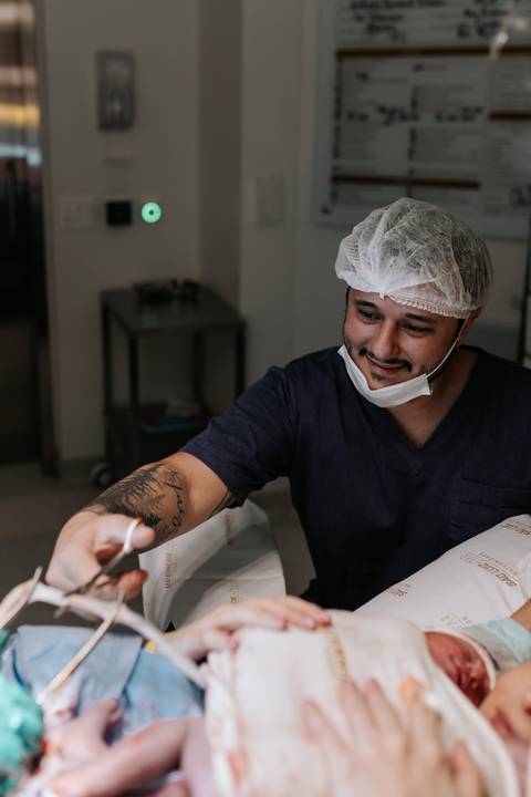Foto do pai sorridente e emocionado, cortando o cordão umbilical.'