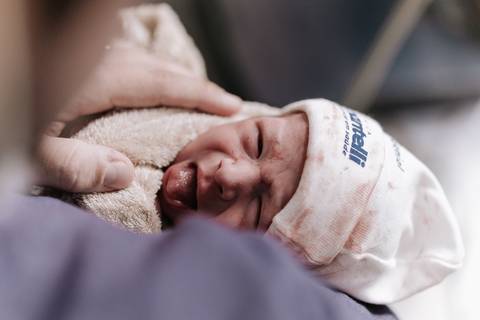 Foto do bebê sendo acolhido em uma manta aquecida logo após o nascimento.'