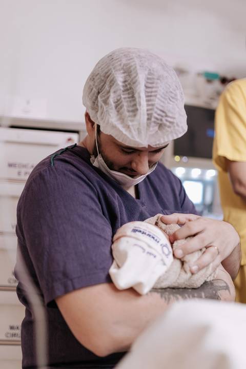 Foto do pai concentrado e emocionado, segurando um dos filhos no colo com todo o cuidado.'