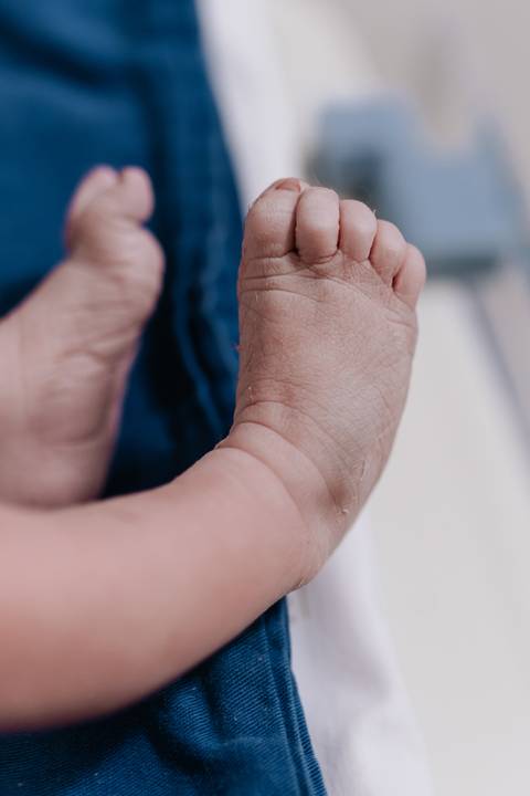 Foto em detalhe focada nas dobrinhas do tornozelo e do pezinho do recém-nascido.'