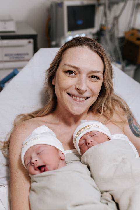 Retrato da mãe sorridente com os dois bebês gêmeos aninhados juntos em seu peito.'