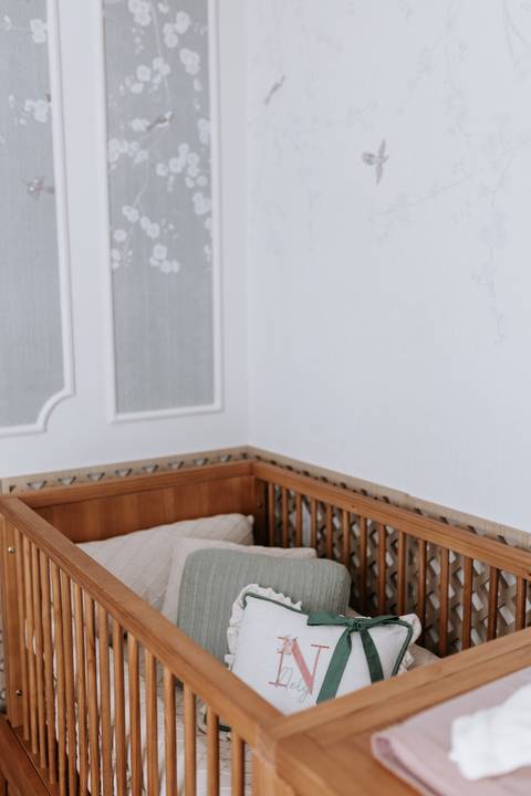 Foto com foco minimalista no berço de madeira clara encostado na parede branca do quarto.'
