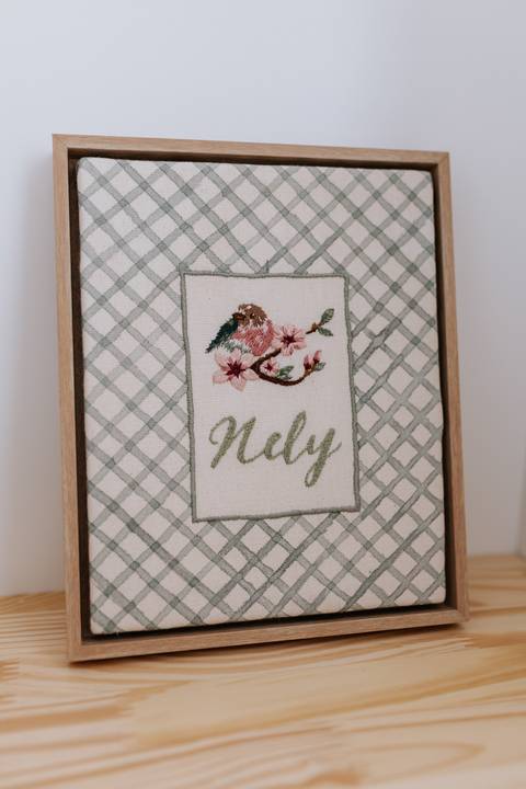 Detalhe de quadro decorativo bordado à mão com ramos de flores e o nome 