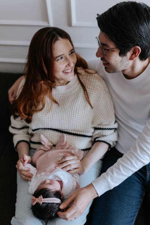 Foto aproximada dos pais com roupas confortáveis, ninando a pequena Nely com carinho.'