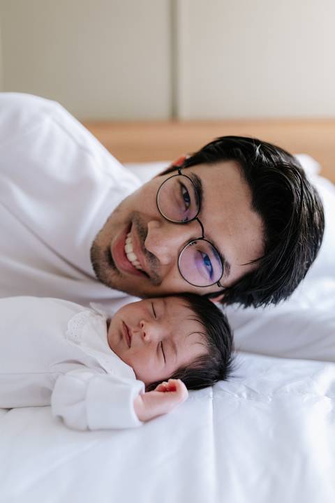 Retrato de close do pai sorridente de óculos posando colado com a filha adormecida.'
