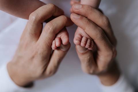 Close focado nos dois pézinhos  sendo amparadas simetricamente pelas mãos do pai.'
