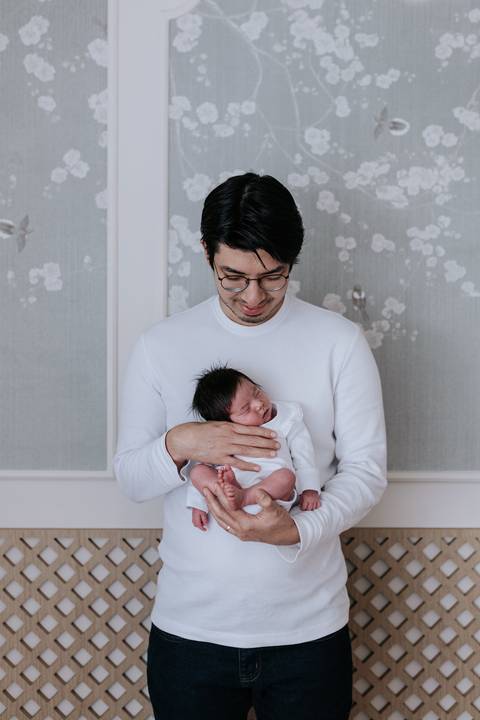 Retrato do pai em pé segurando a bebê adormecida com cuidado em seus braços.'