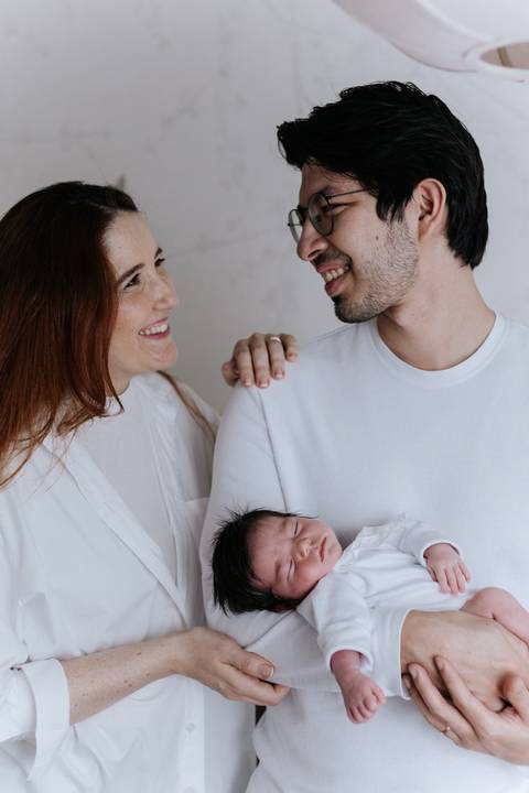 Retrato de perfil do casal sorrindo um para o outro enquanto o pai segura a filha no colo.'