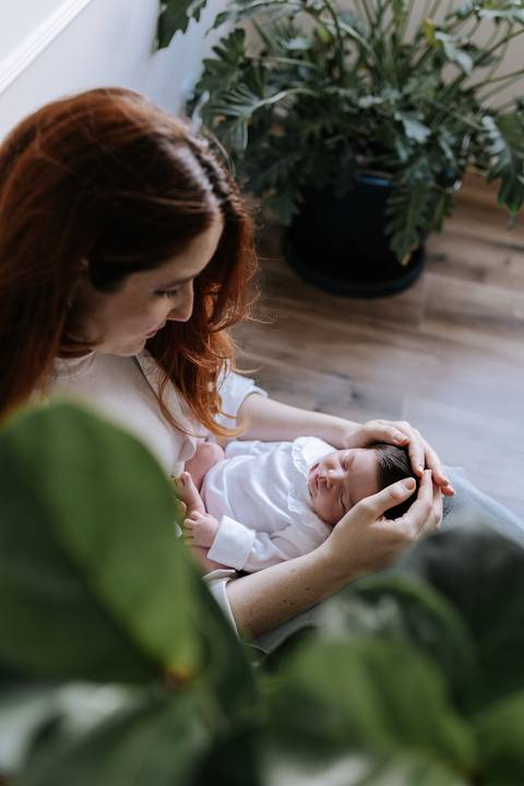 Foto de ângulo superior da mãe sentada com a bebê deitada em seu colo, acariciando sua cabecinha.'