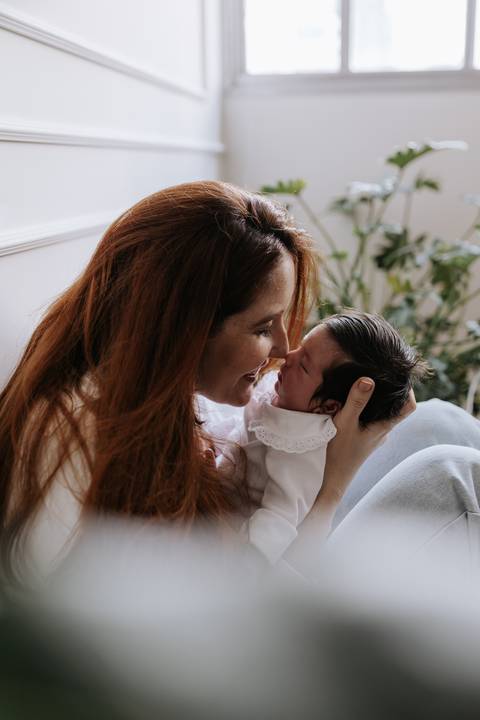 Retrato aproximado da mãe com o rosto colado ao da bebê, compartilhando um momento de carinho.'